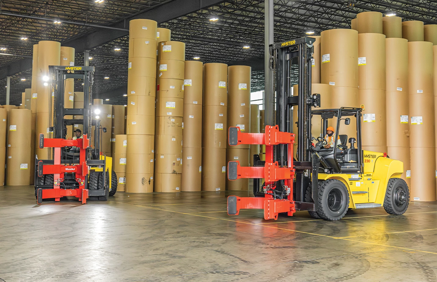Two Hyster lift trucks with red Bolzoni paper roll clamp attachments.